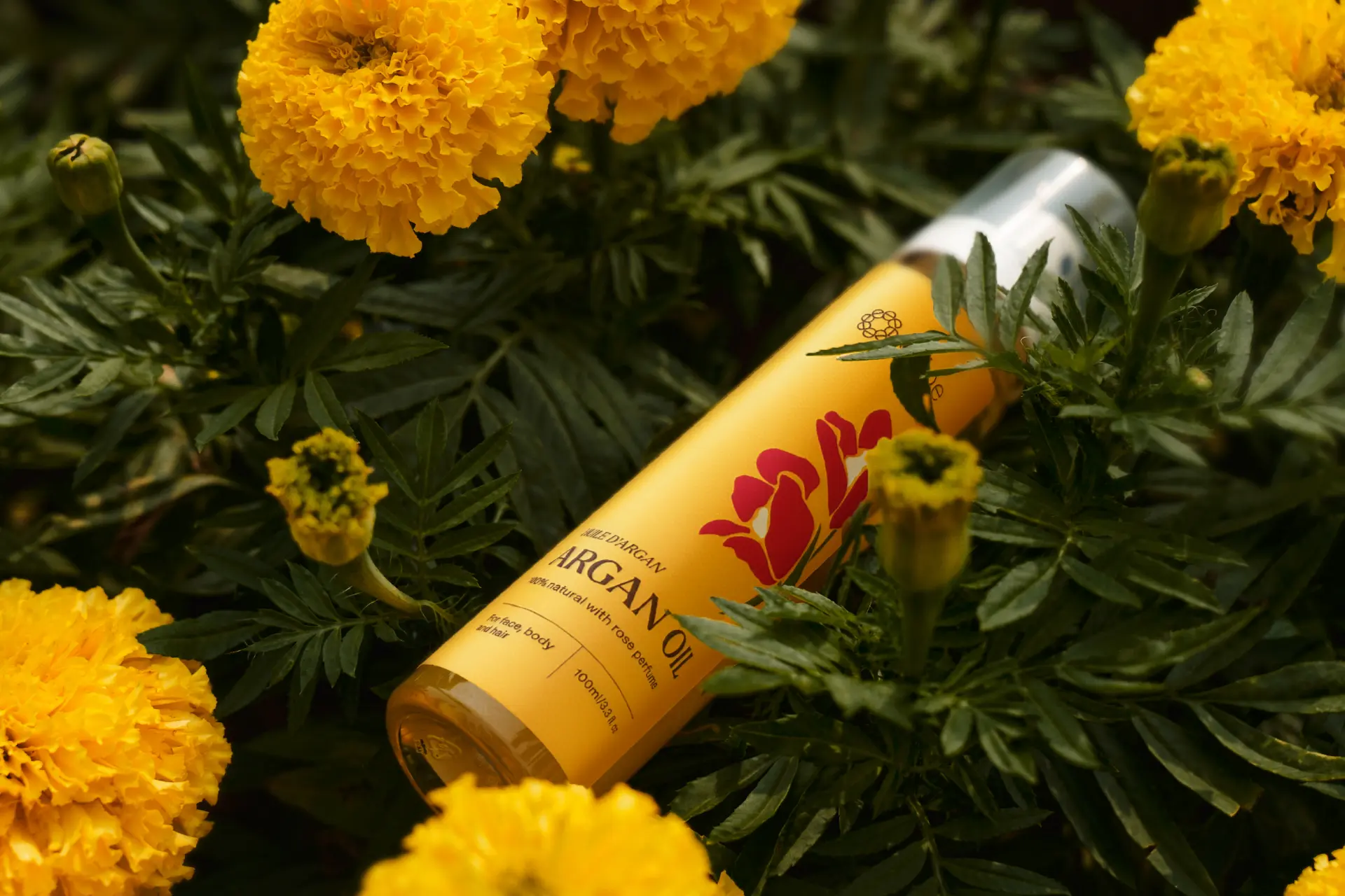 e'lioe rose argan oil bottle resting among yellow marigold flowers