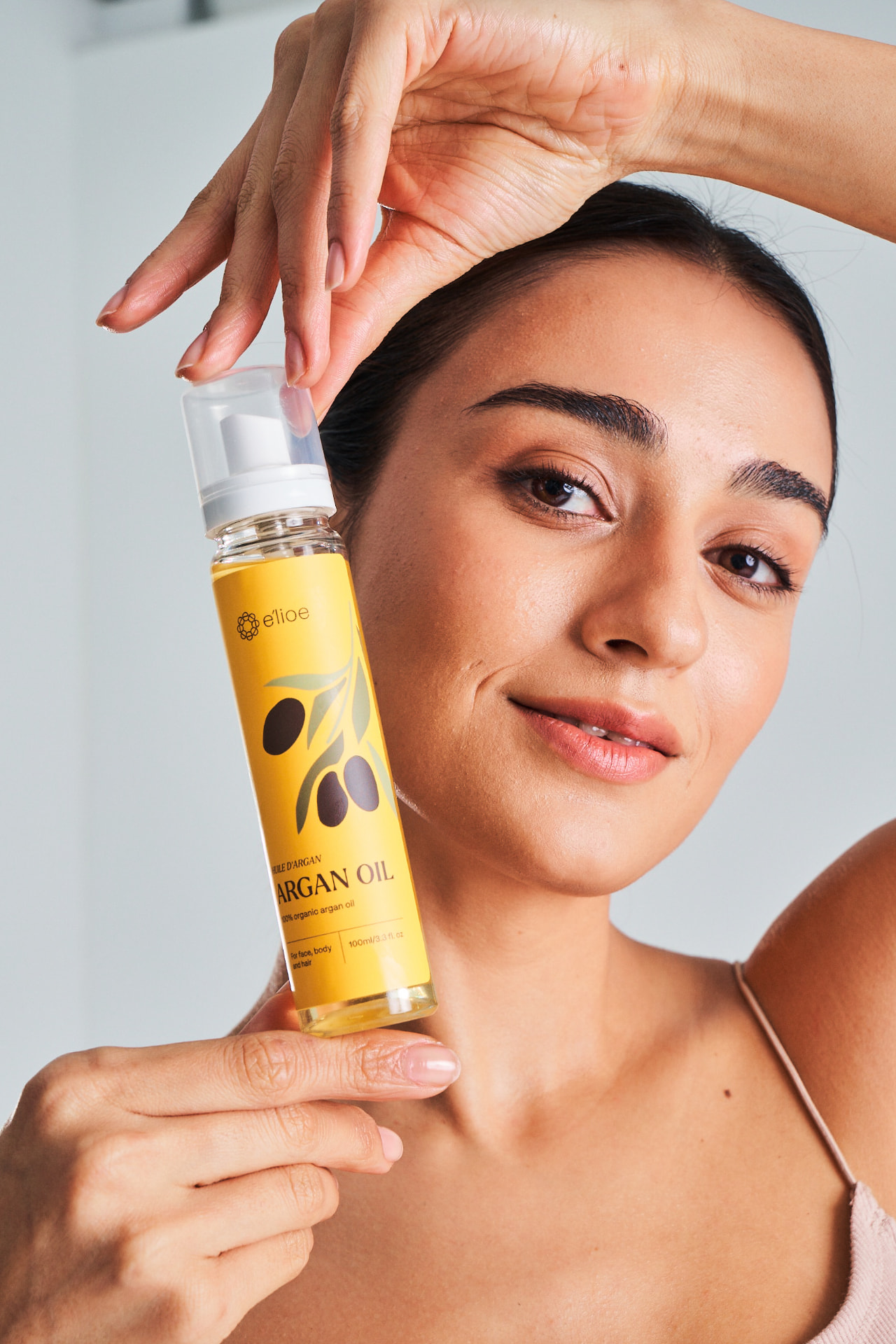 Woman with glowing skin holding a bottle of e'lioe argan oil beside her face