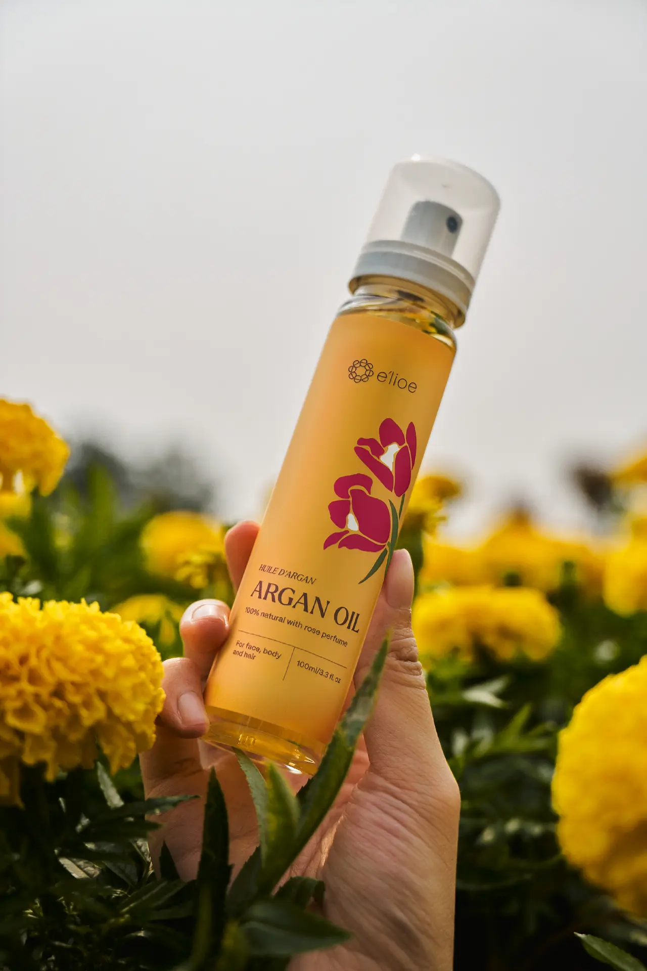 Hand holding an e'lioe rose argan oil bottle in a marigold field