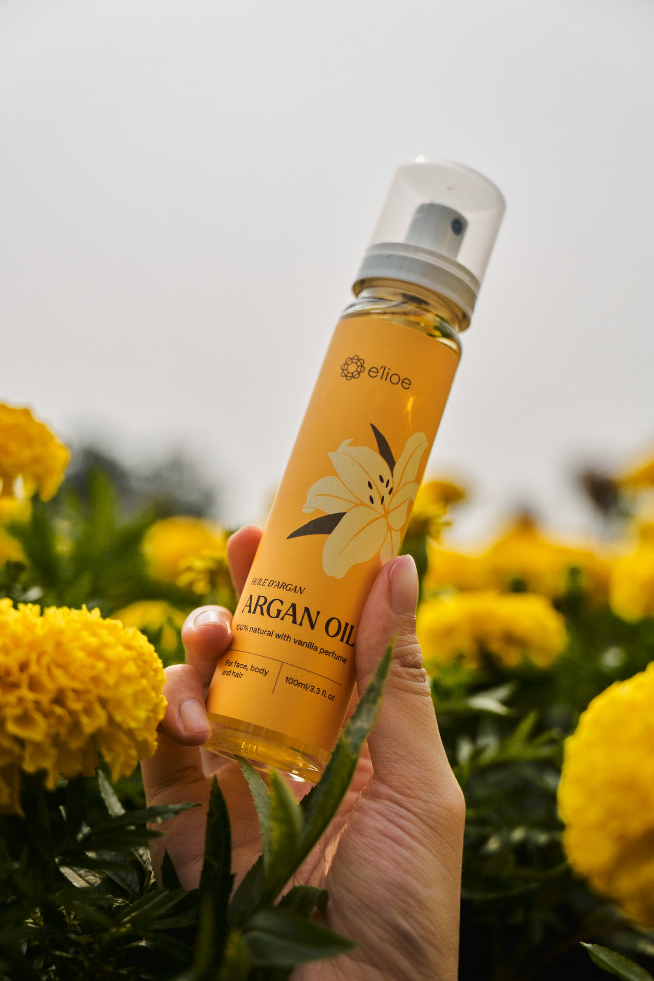 Hand holding an e'lioe argan oil bottle in a marigold field